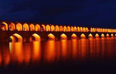 Illuminated bridge over river against sky at night