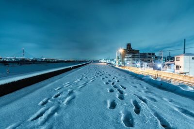 Snow covered illuminated factory against sky during winter