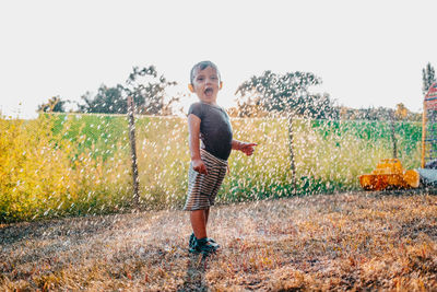 Full length portrait of boy standing on grass amidst sprinkled water