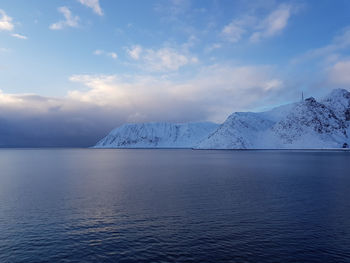 Scenic view of sea by snowcapped mountain against sky