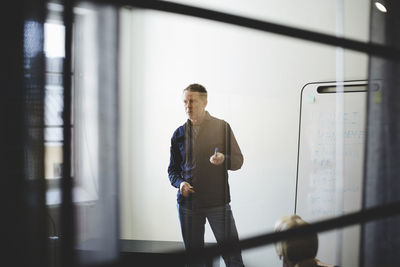 Businessman standing against white wall in board room seen from glass at creative office