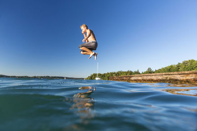 Shirtless man jumping on sea against clear blue sky