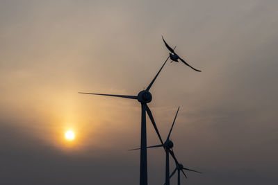 Low angle view of wind turbines against sky during sunset