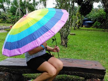 A woman sitting on a wooden bench with a rainbow umbrella