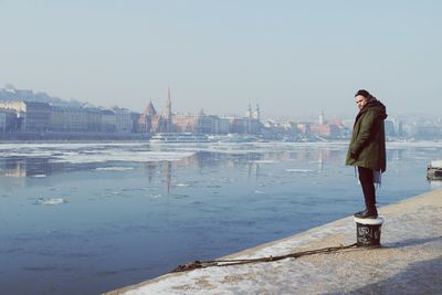 Man standing on bollard by lake in city