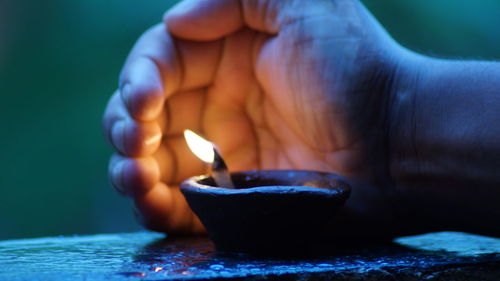 Cropped hand shielding burning diya on retaining wall