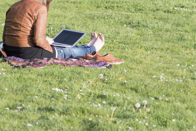Low section of woman using laptop while sitting on grassy field