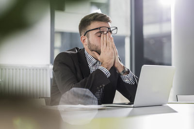 Exhausted young man with laptop in office