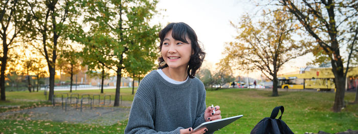 Young woman looking away while standing against trees