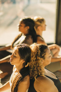 Women friends sitting back to back and exercising during yoga class