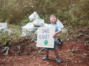 Full length of smiling girl holding cardboard with text save planet