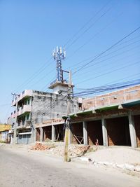 Low angle view of electricity pylon and buildings against clear sky