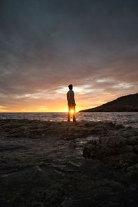 Rear view of silhouette man standing on coast during sunset