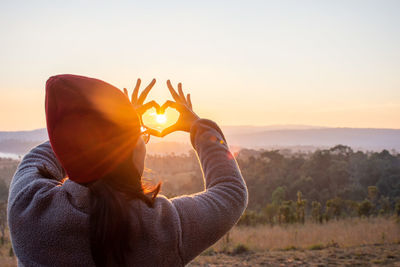 Rear view of woman with arms raised against sky during sunset