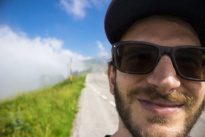 Close-up portrait of smiling bearded man wearing sunglasses against sky