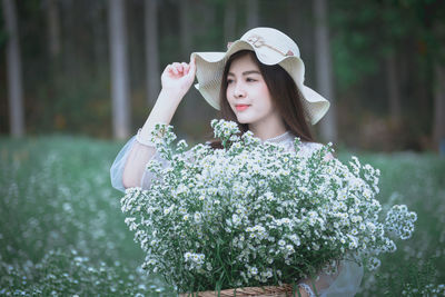 Beautiful young woman wearing hat while holding flowering plants