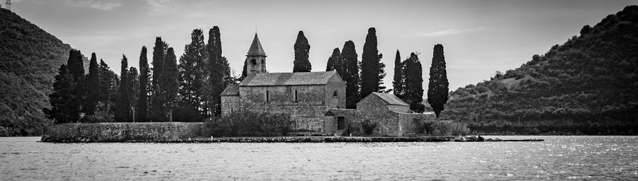 Old church by bay of water against sky