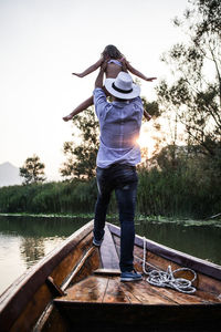 Full length of father carrying daughter while standing on boat over lake against sky