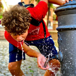 Portrait of boy drinking water at fountain at park