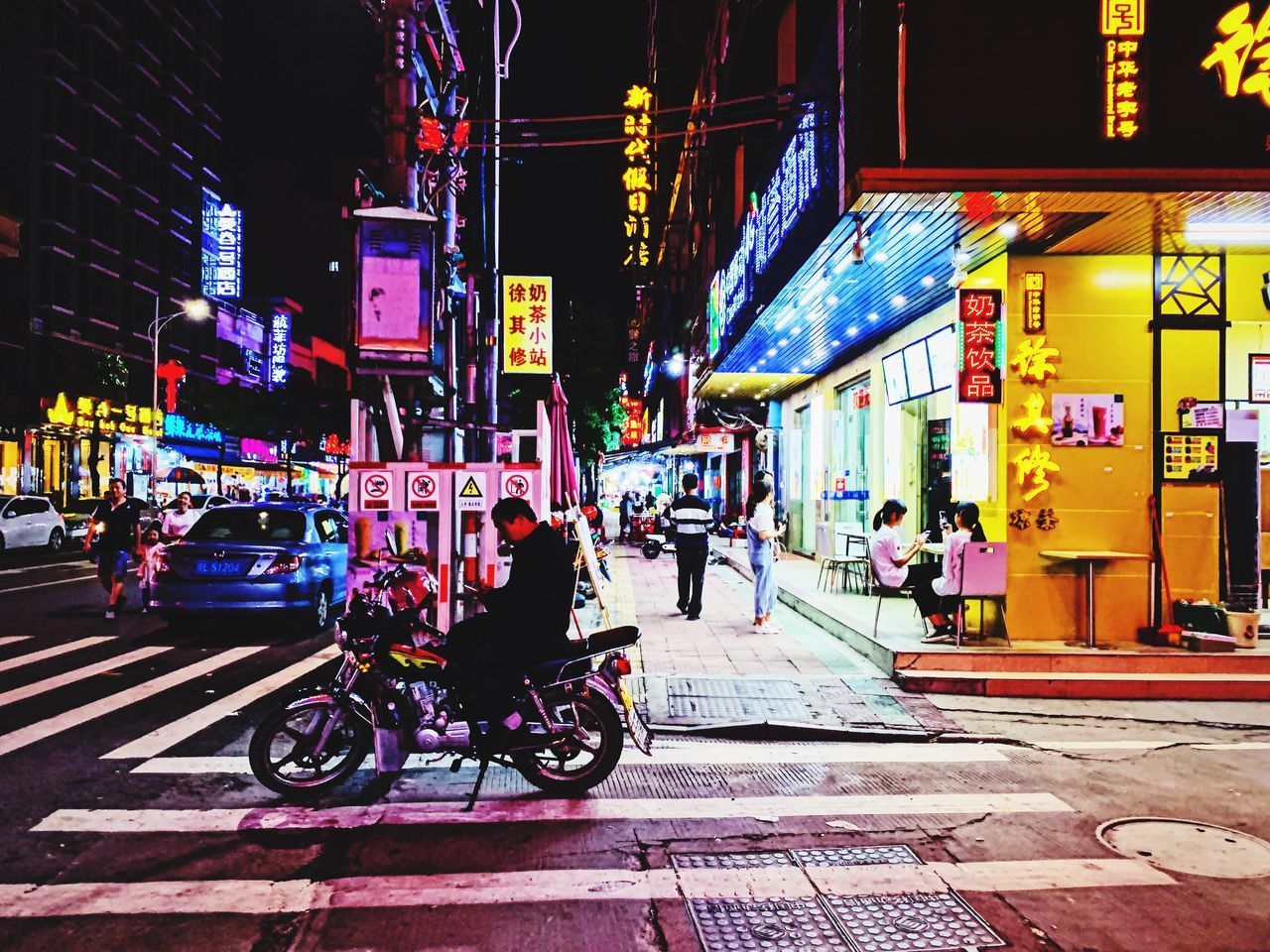 PEOPLE ON STREET AMIDST ILLUMINATED CITY BUILDINGS