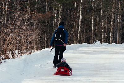 Woman with baby boy walking on snow against bare trees