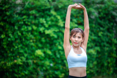 Young woman with arms raised against trees