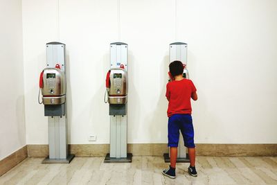 Rear view of boy using pay phone against wall