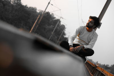 Man sitting on car against sky