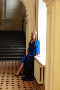 Portrait of beautiful young model wearing crown while sitting in corridor