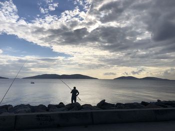 Silhouette man fishing in sea against sky