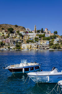 Sailboats moored in sea by buildings against clear blue sky