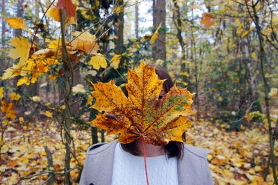 Close-up of woman with orange maple leaf in forest during autumn