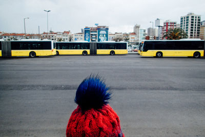 Cropped image of person wearing knit hat against buses on city street