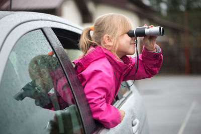 Sid view of girl looking through binoculars while traveling in car