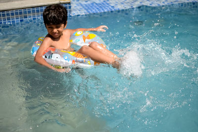 Happy indian boy swimming in a pool, kid wearing swimming costume along with air tube during day