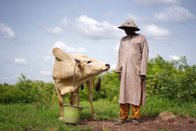Farmer standing by cow at field