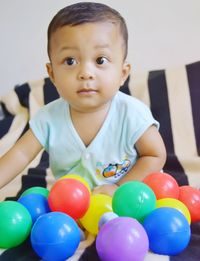 Cute boy sitting by balls on bed at home