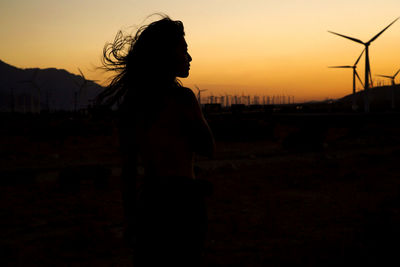 Silhouette of woman in front of wind farm at sunset