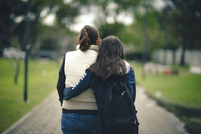 Rear view of mother and daughter embracing on footpath