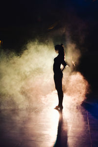 Silhouette of a woman dancing between lights and smoke unrecognozible person