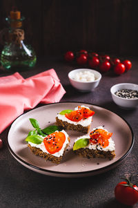 Appetizing crostini on rye bread with ricotta and tomatoes on a plate vertical view