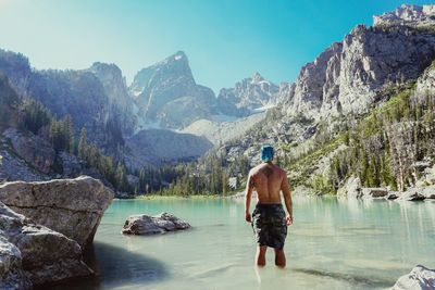 Rear view of shirtless man standing in lake against rocky mountains