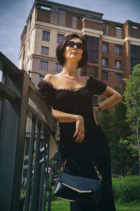 A pretty charming middle-aged woman in a black dress and sunglasses strolls through the city street