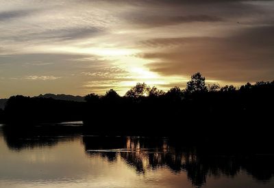 Silhouette trees by lake against sky during sunset