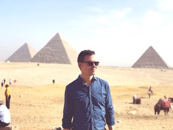 Man looking away while standing against pyramid at desert