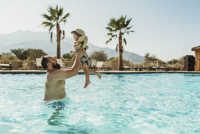 Father throwing young boy up in air while playing in pool on vacation