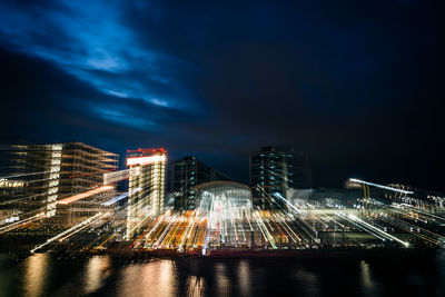 Illuminated buildings at waterfront against sky at night