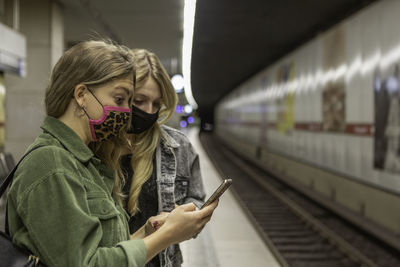 Full length of young woman using mobile phone on railroad platform