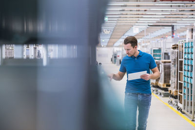 Man with tablet looking at tugger train in industrial hall