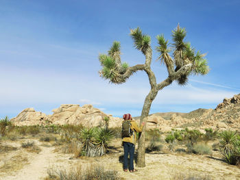 Man by tree on land against sky